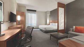 A hotel room with a bed, a desk with a chair, a TV, and a sofa.