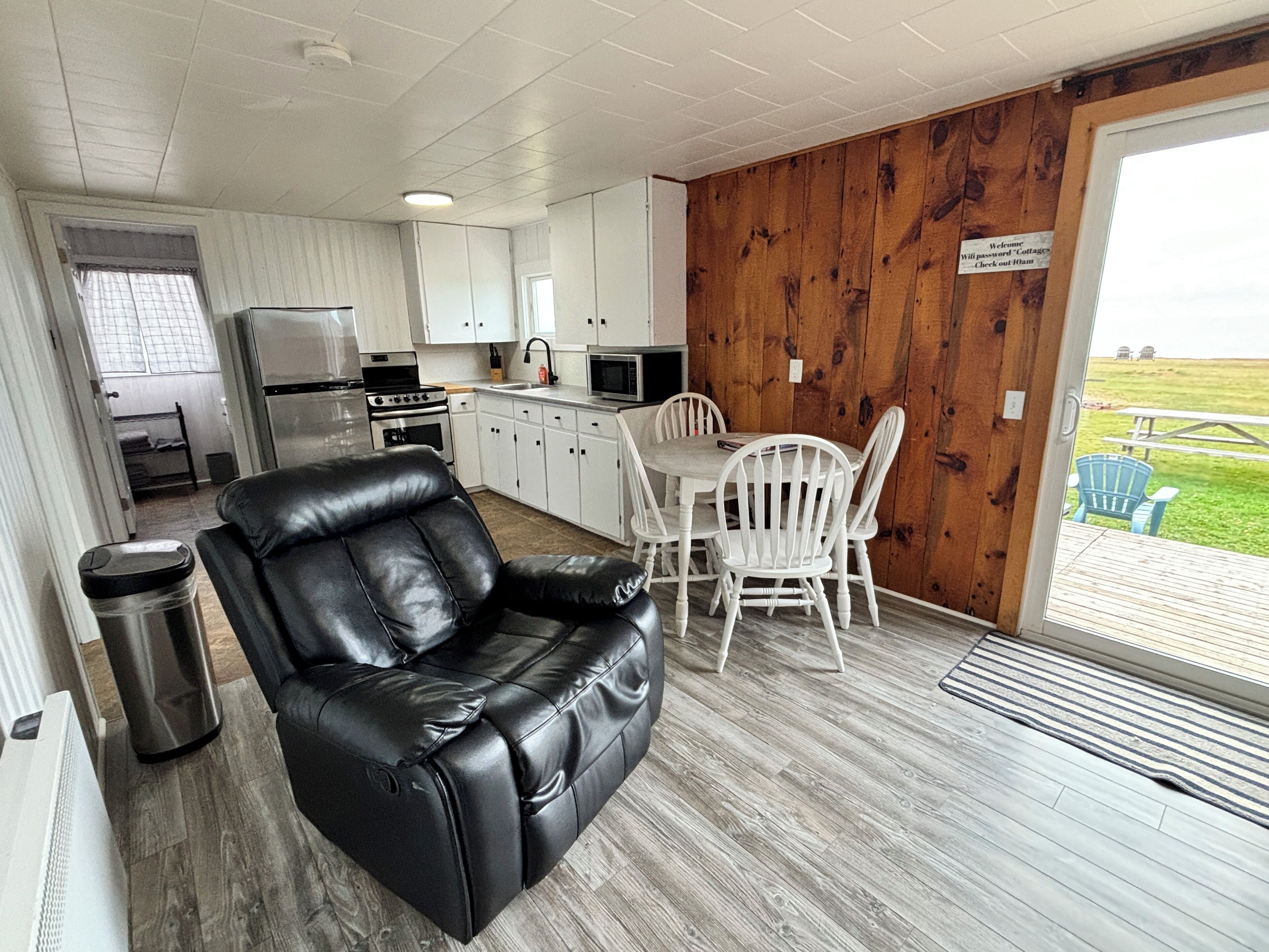 A modern kitchen with white cabinets, a stainless steel refrigerator, and a dining area with white chairs and a table.