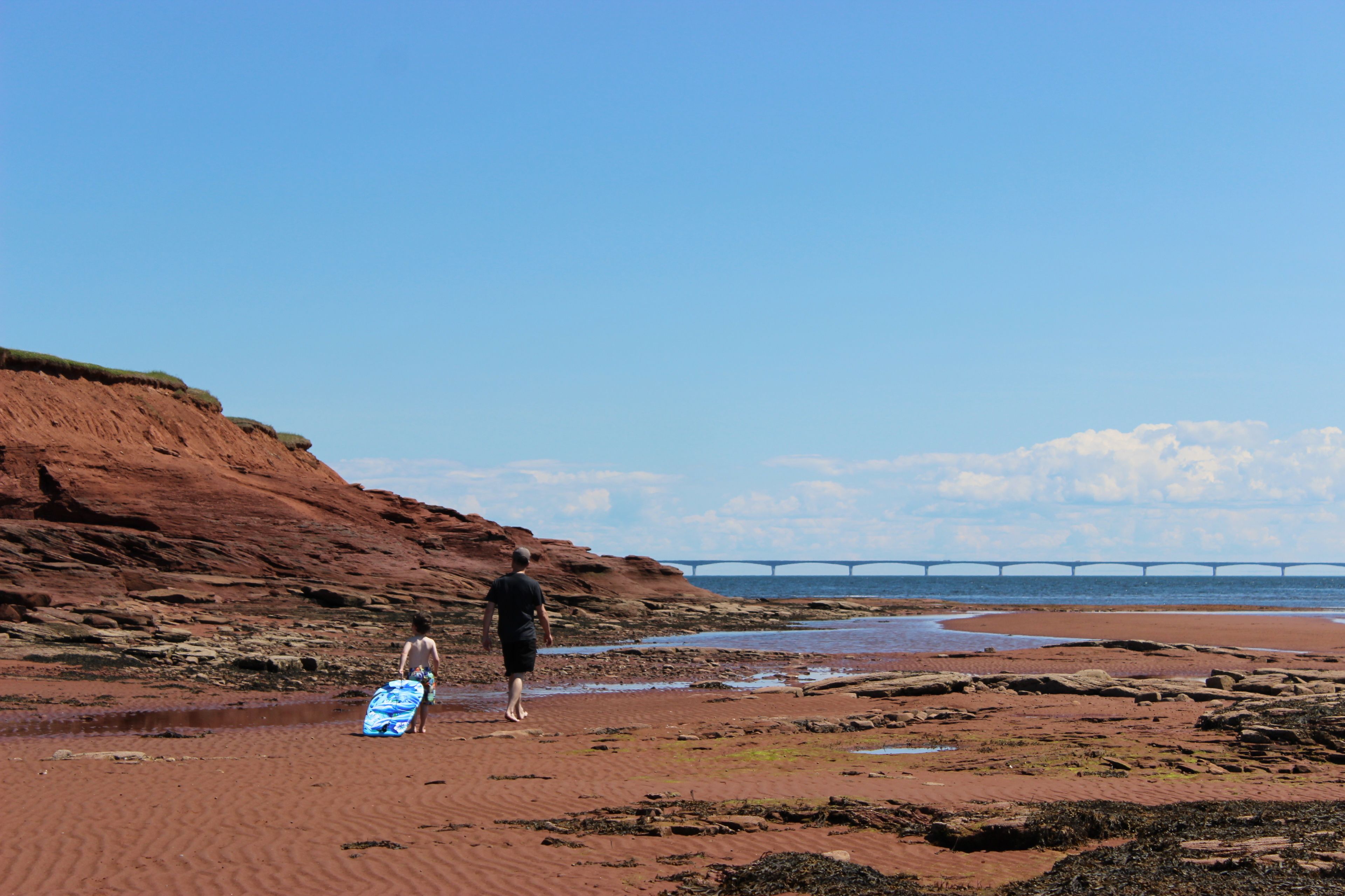 A beach with a person walking towards the water, carrying a surfboard.