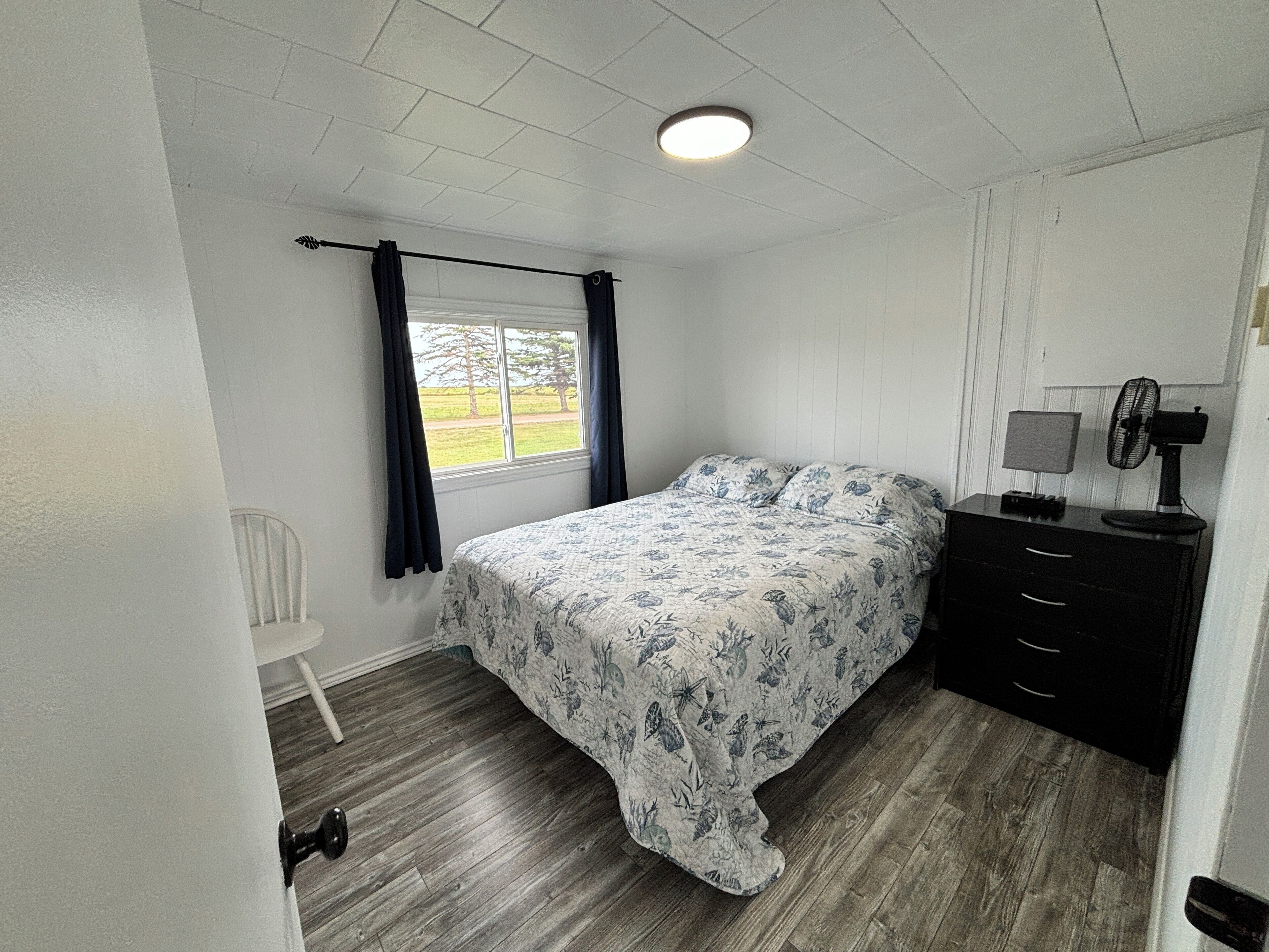 Une chambre à coucher avec un lit, une commode, une chaise et une fenêtre avec des rideaux.
