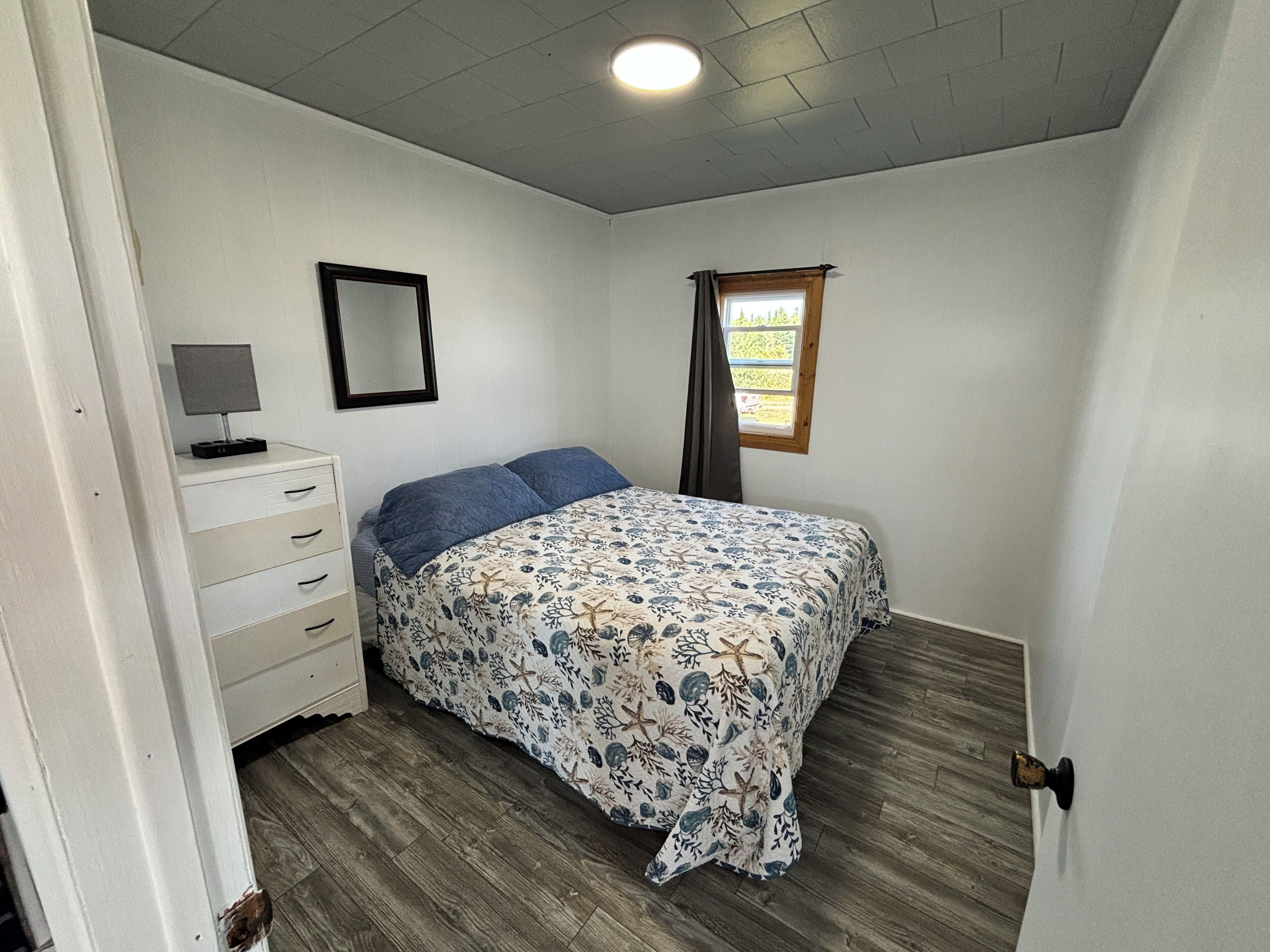 Een slaapkamer met een bed, een dressoir, een spiegel en een raam met gordijnen.
