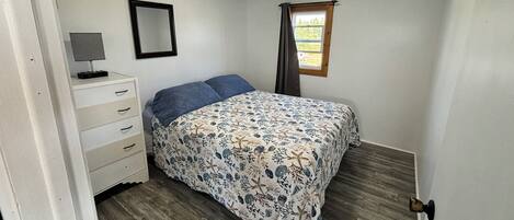 Een slaapkamer met een bed, een dressoir, een spiegel en een raam met gordijnen.
