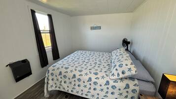Ein kleines Zimmer mit einem Einzelbett, das mit einem Bezug im maritimen Stil ausgestattet ist, einem Nachttisch mit Lampe, einem Fenster mit Vorhängen und einem an der Wand befestigten Ventilator.