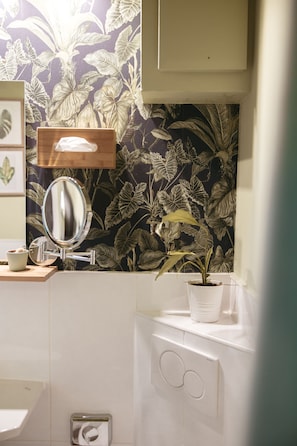 A bathroom with a mirror, a sink, a toilet paper holder, and a potted plant. - Hotel North (Hamburg)