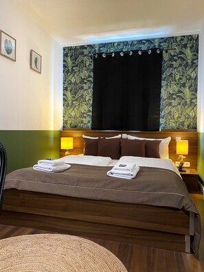 A hotel room with a large bed, two bedside lamps, a headboard with a floral wallpaper, and a window with a curtain. - Hotel North (Hamburg)