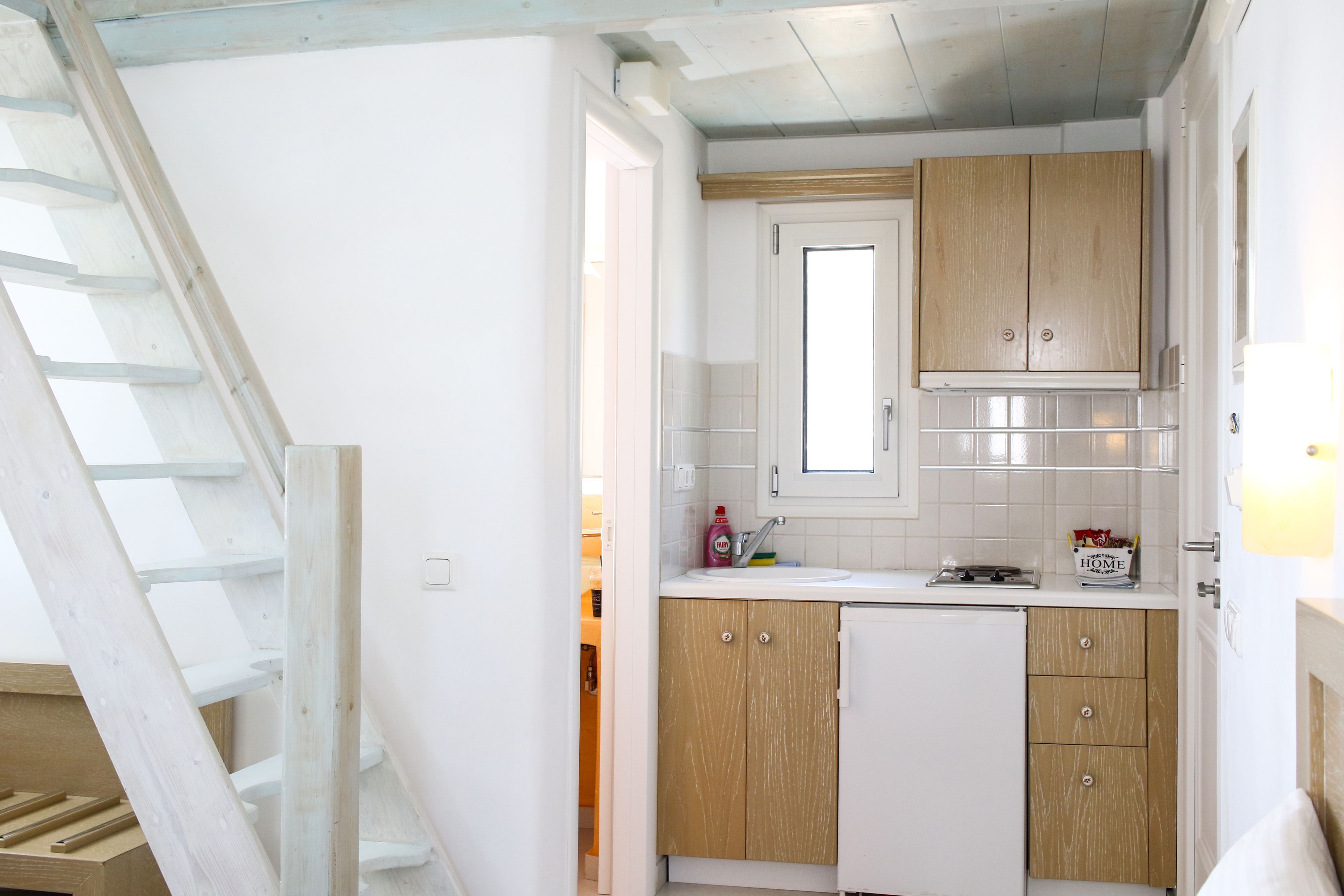 A compact kitchen with wooden cabinets, a white countertop, and a window above the sink.