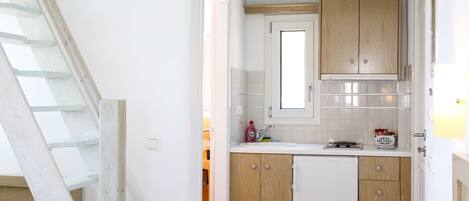 A compact kitchen with wooden cabinets, a white countertop, and a window above the sink.