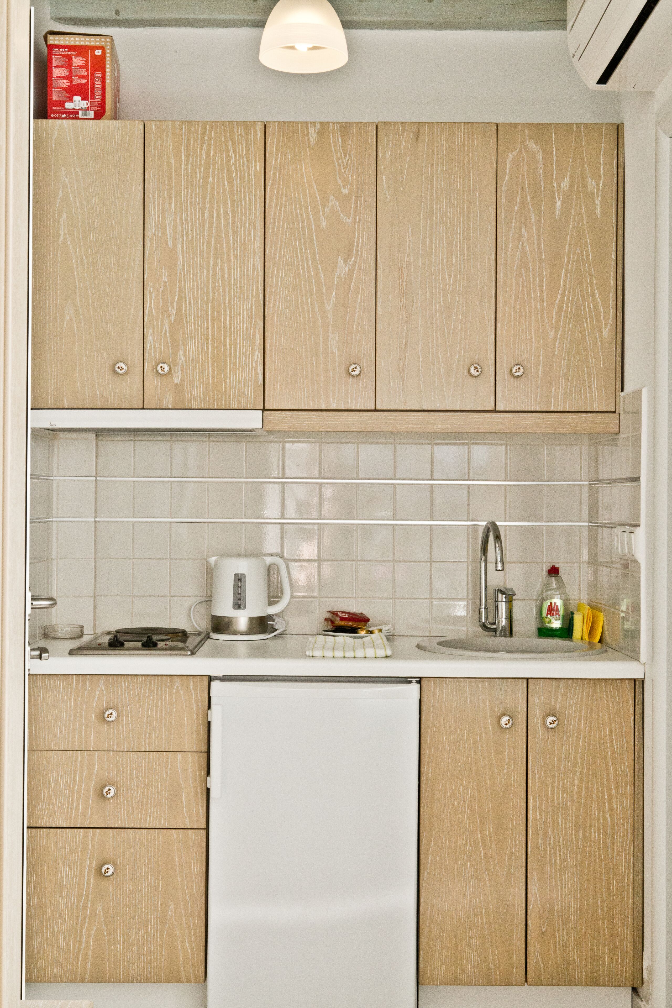 A kitchen with wooden cabinets, a white refrigerator, a kettle, a sink, and a bottle of dish soap.