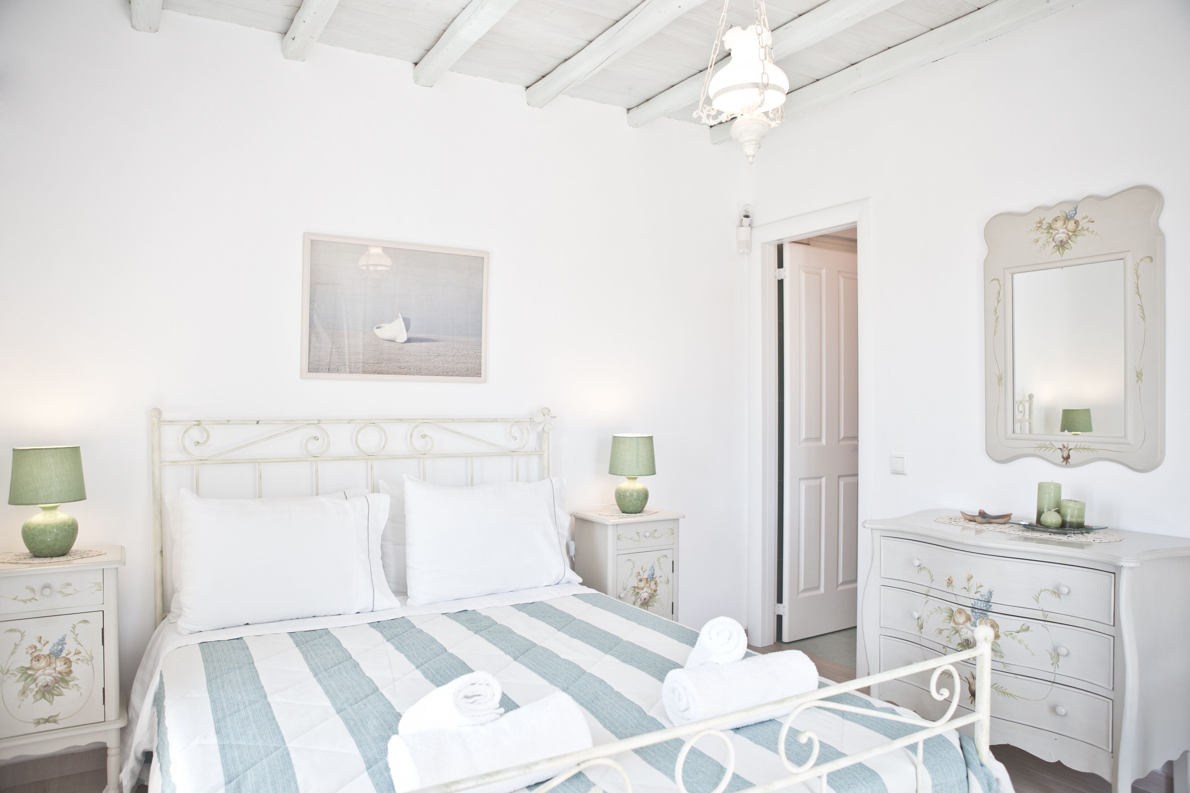 Une chambre à coucher avec un lit, deux tables de chevet, une commode, un miroir et un tableau accroché au mur.