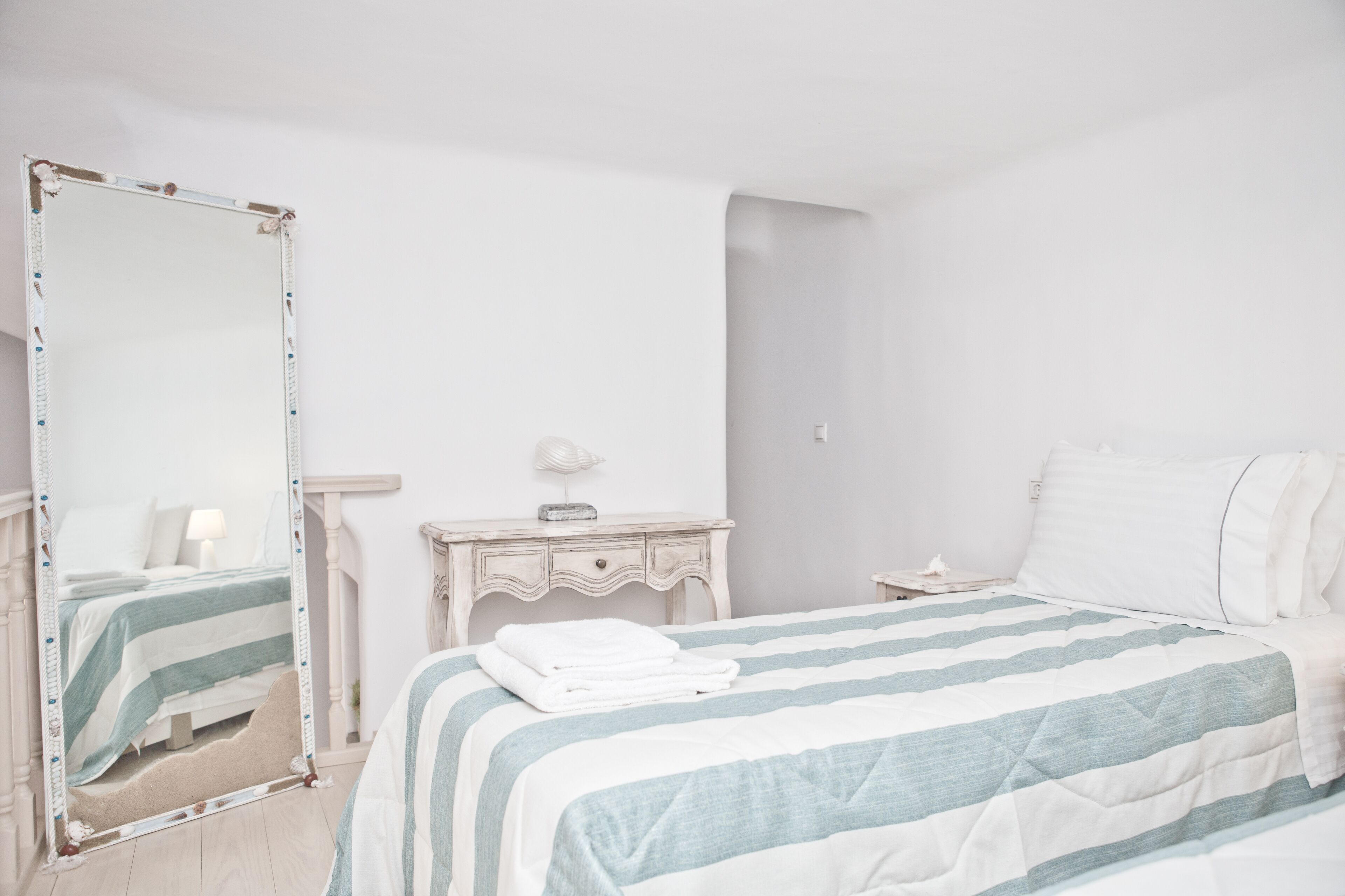 Un dormitorio con cama, cómoda, mesita de noche y un espejo grande.