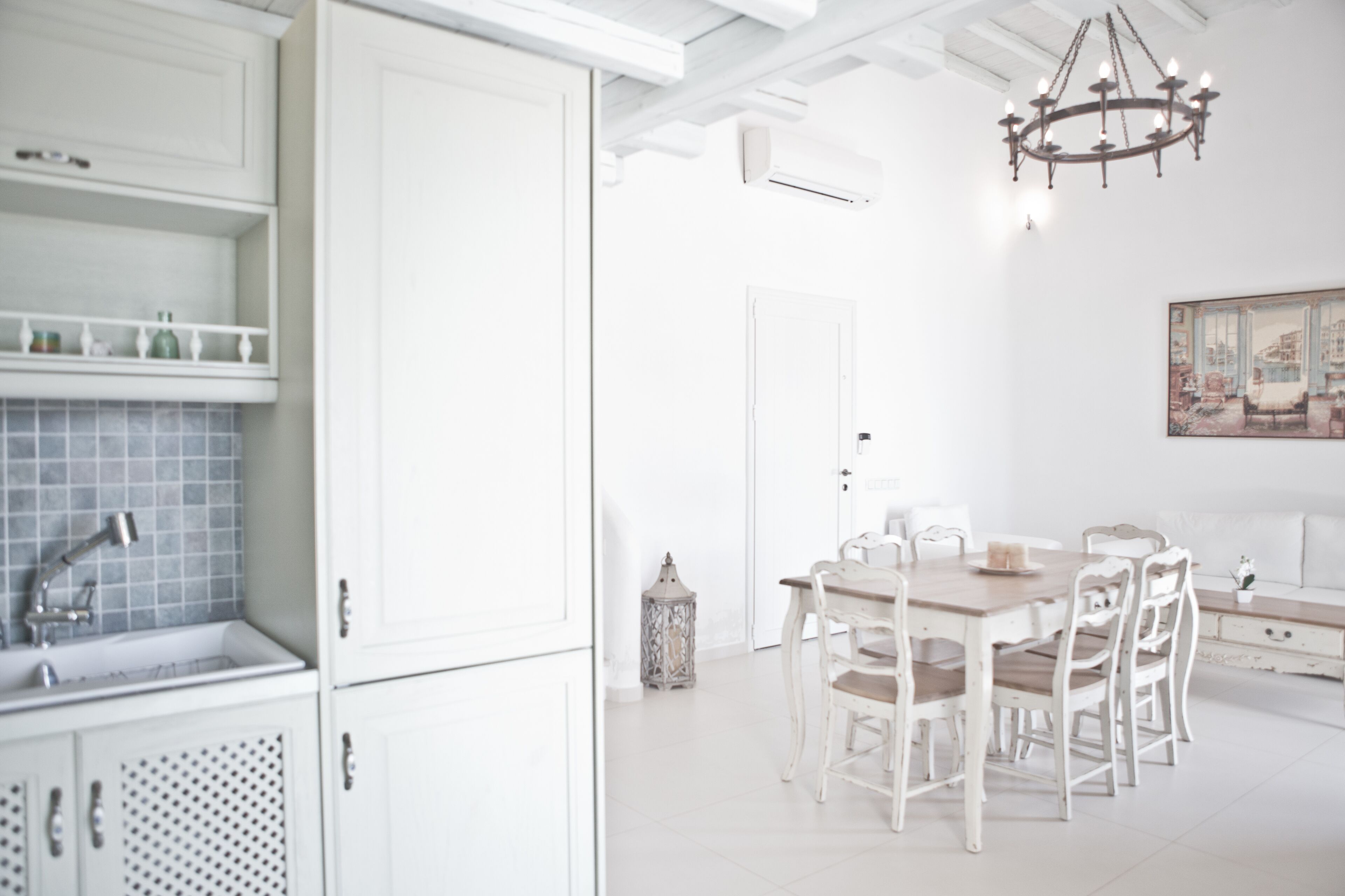 A bright, white interior with a dining area, white cabinets, and a chandelier.
