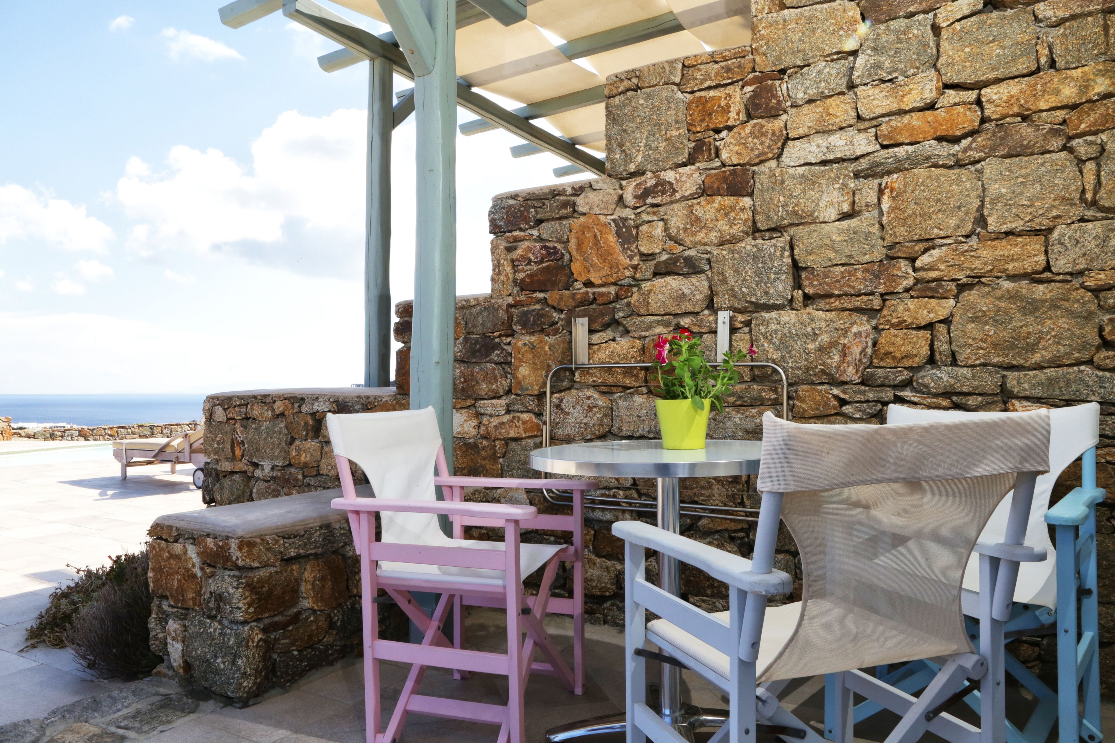 Un mur de pierre donnant sur la mer, une table avec des chaises et une plante en pot.