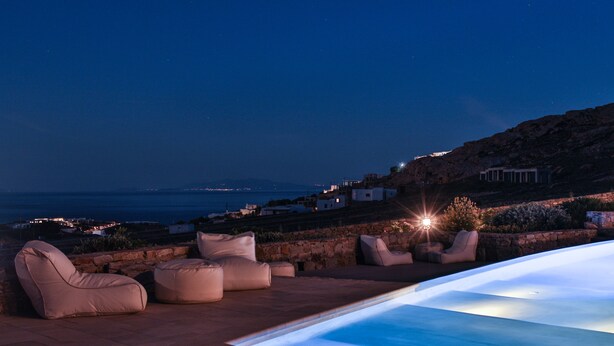 A rooftop pool area with seating and a view of the coastline at night. - Niriides Homes & Villas (Mykonos)