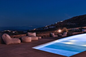 A rooftop pool area with seating and a view of the coastline at night. - Niriides Homes & Villas (Mykonos)