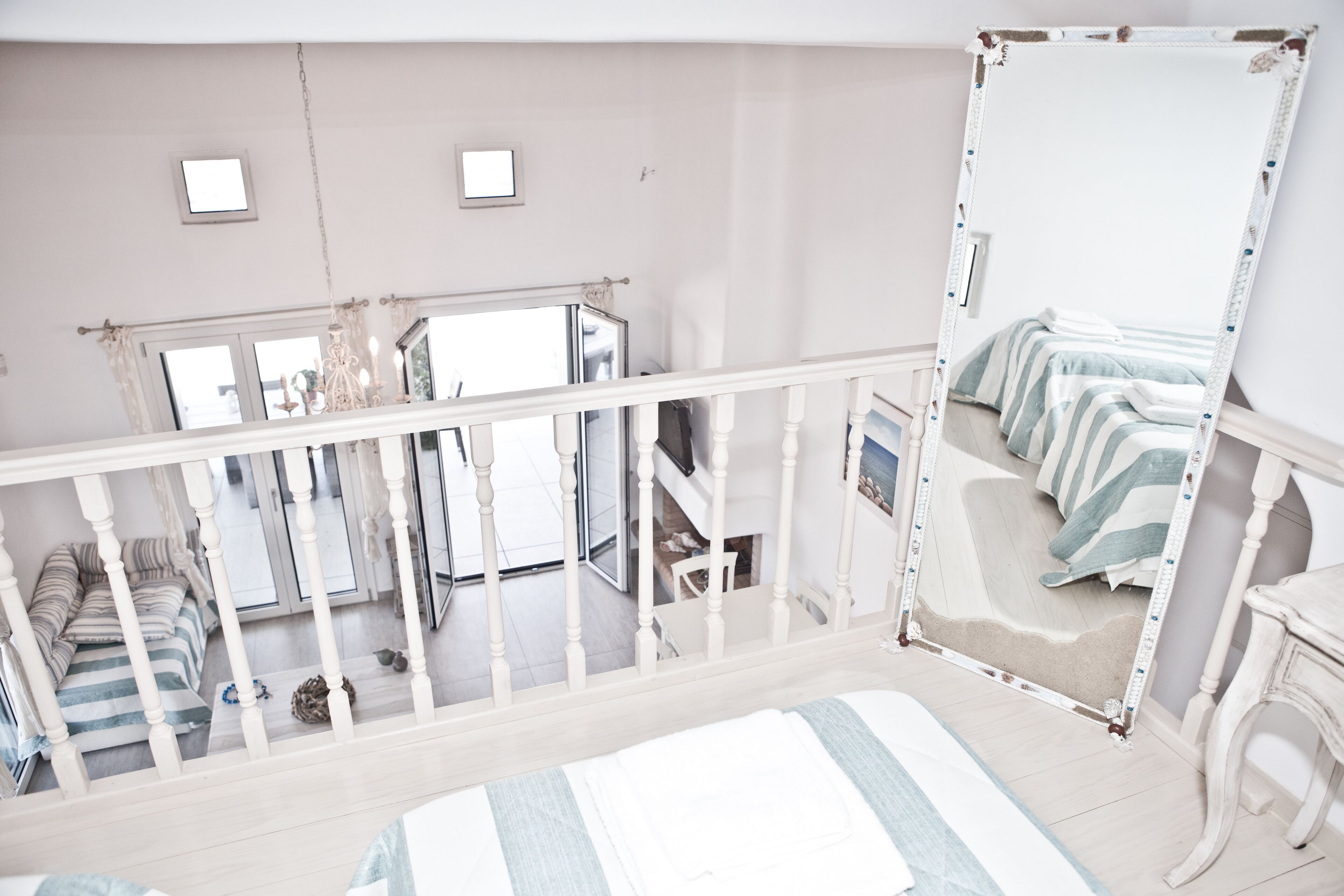 A bedroom with a large bed, a white railing, a mirror, and a view of a balcony.