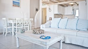 A white living room with a white sofa, a coffee table, and a dining area with white chairs and a white table. - Niriides Homes & Villas (Mykonos)