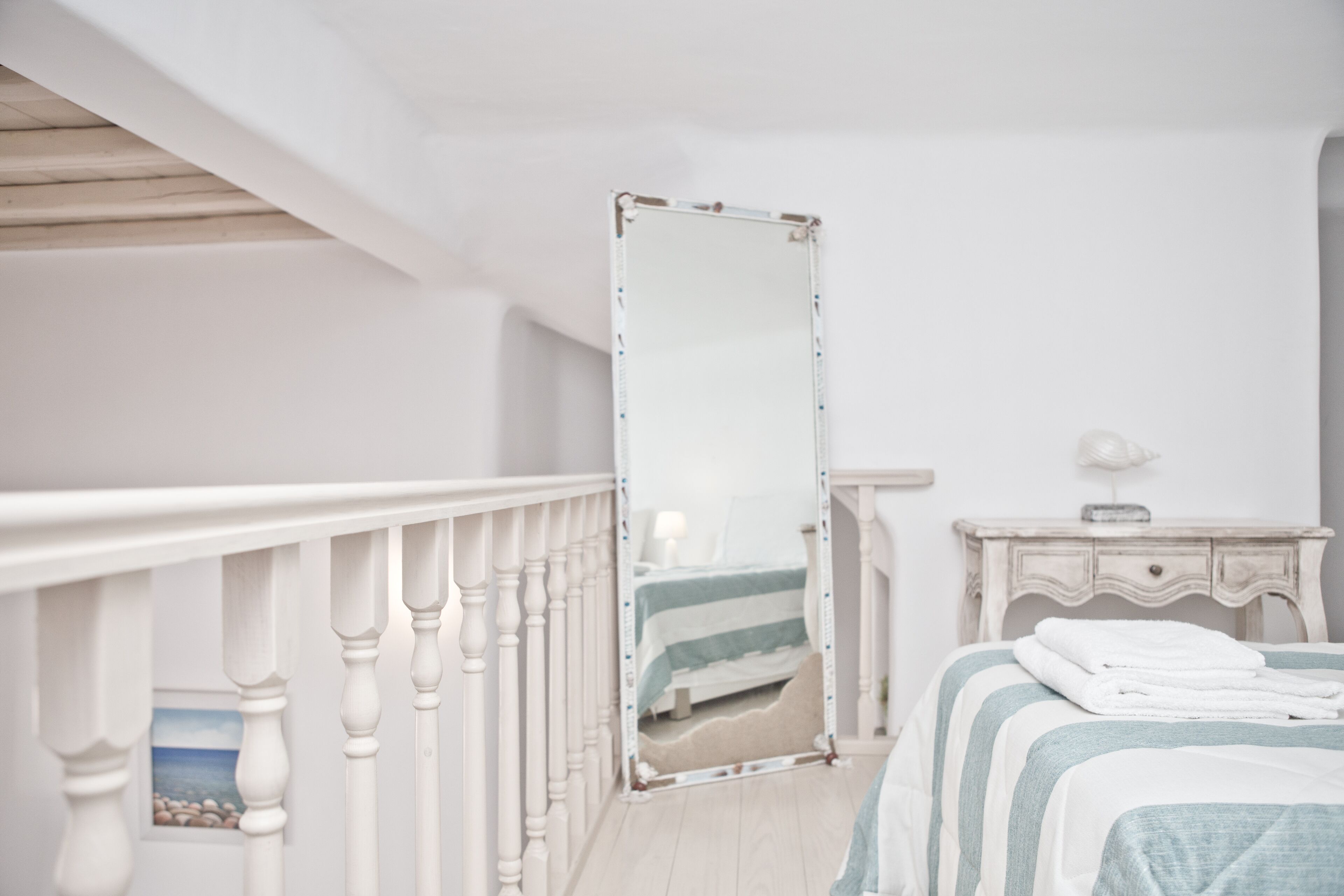 A bedroom with a bed, a bedside table, a mirror, and a view of the beach through a window.
