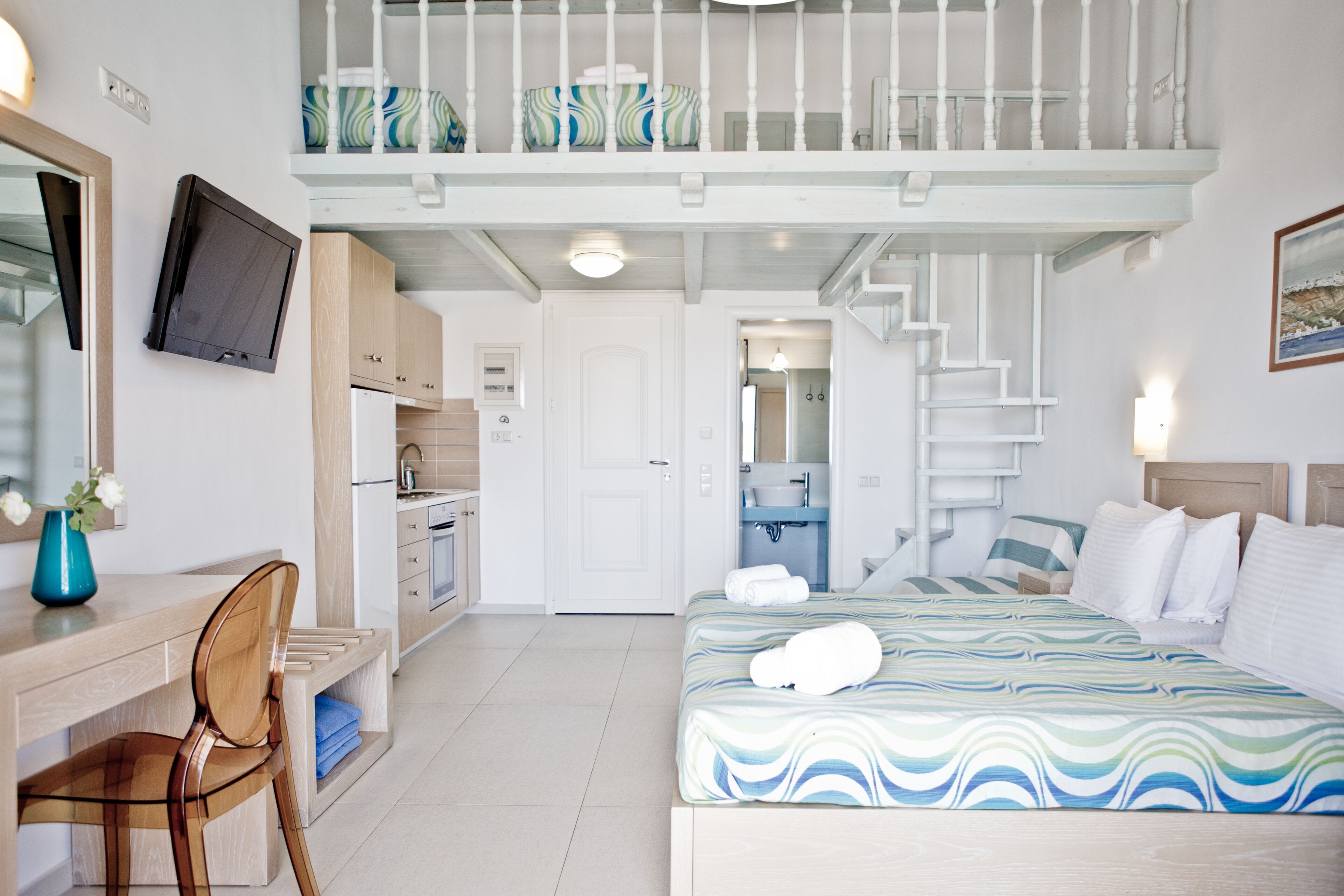 A hotel room with a bed, a desk, a chair, a TV, a balcony, and a bathroom.