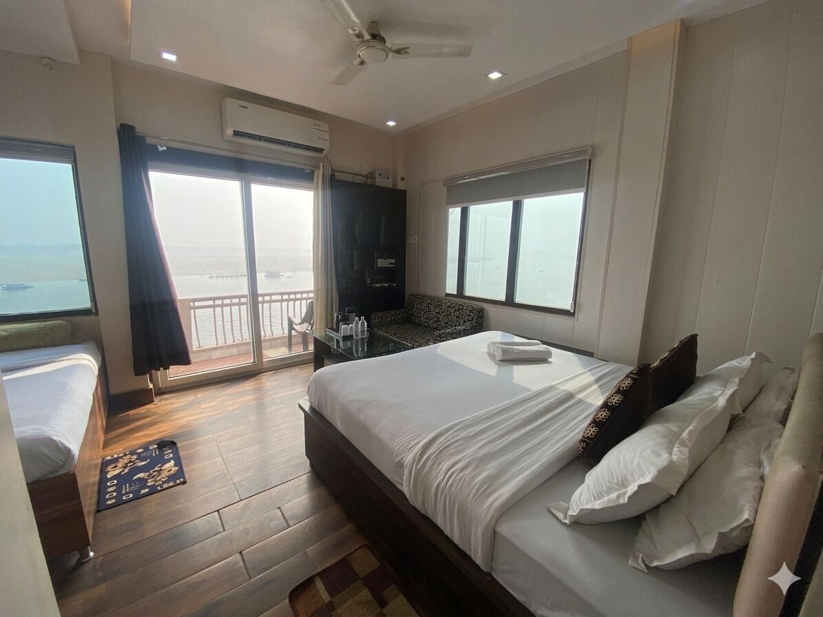 A hotel room with a bed, a small table, a chair, a window, and an air conditioning unit.