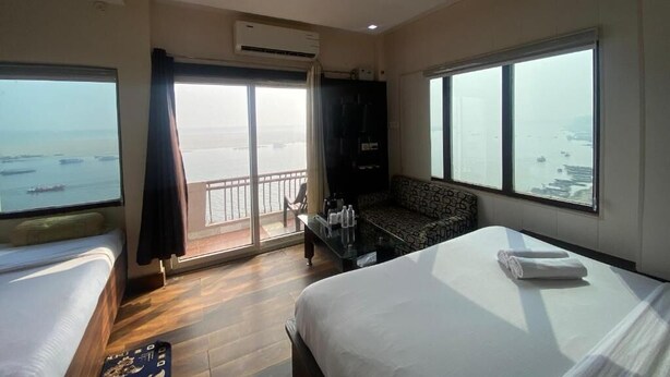 A hotel room with a bed, a sofa, a balcony with a view of the sea, and an air conditioning unit. - Hotel Sita (Varanasi)