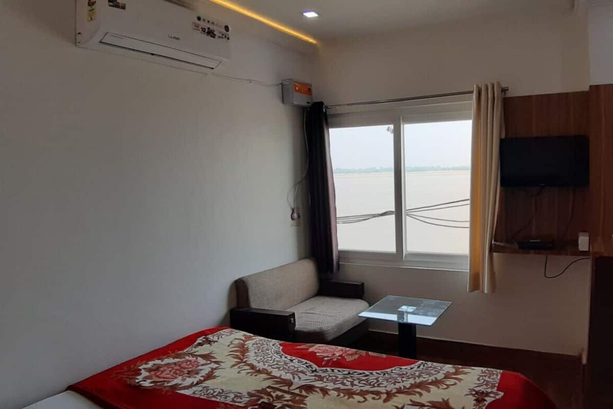 Habitació d'hotel amb llit, taula petita, sofà, televisió penjada a la paret i finestra amb vista a l'aigua.