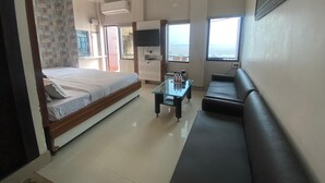 A hotel room with a bed, a sofa, a TV, and a window with a view. - Hotel Sita (Varanasi)