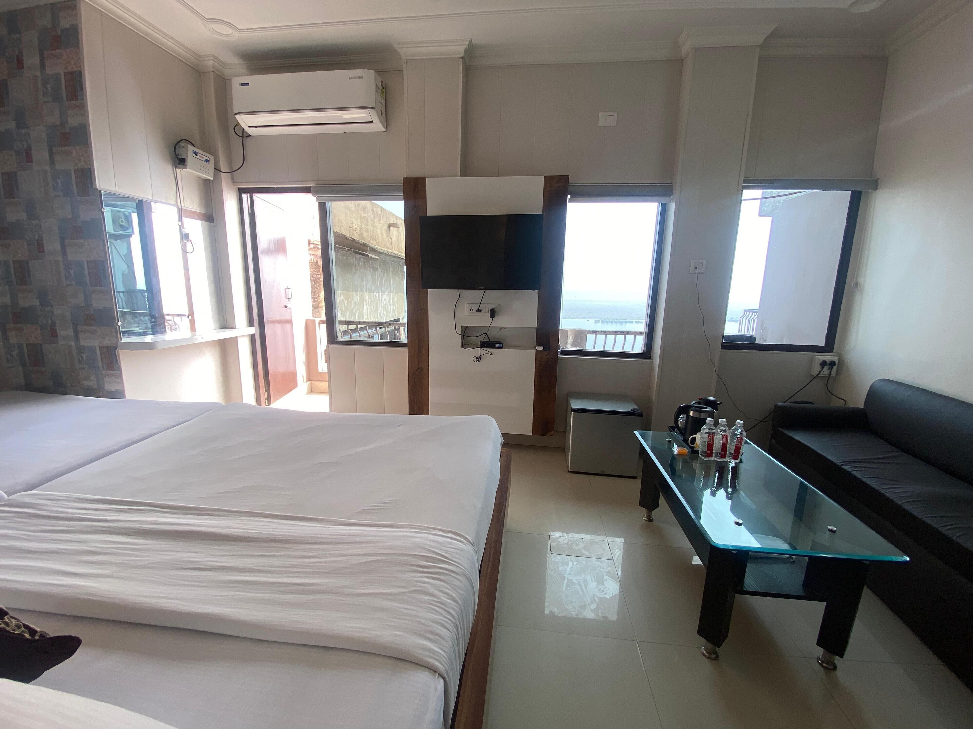 A hotel room with a large bed, a small kitchenette, a glass table, and a sofa.