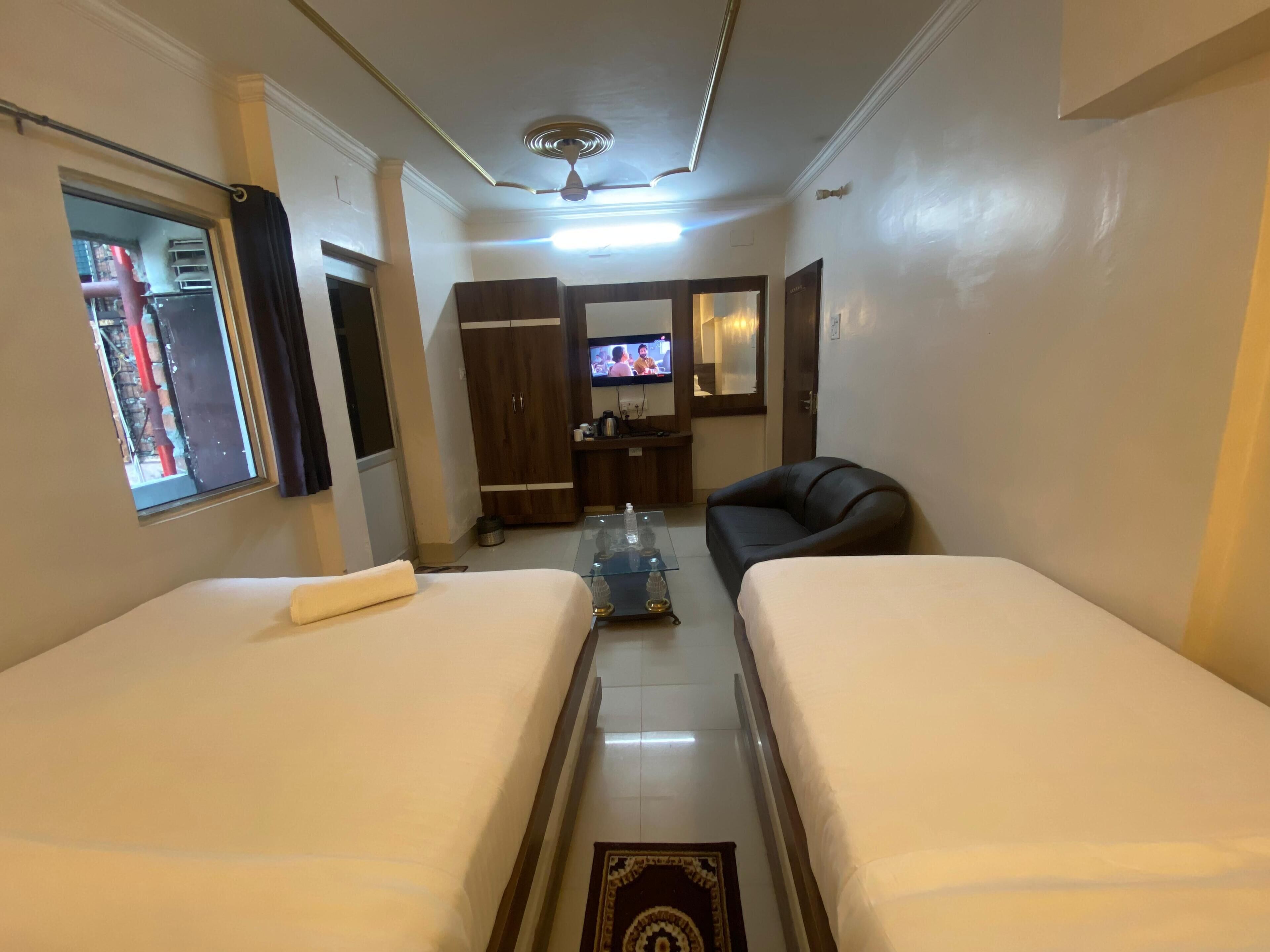 Een hotelkamer met twee bedden, een televisie, een kledingkast en een klein bureau met spiegel.