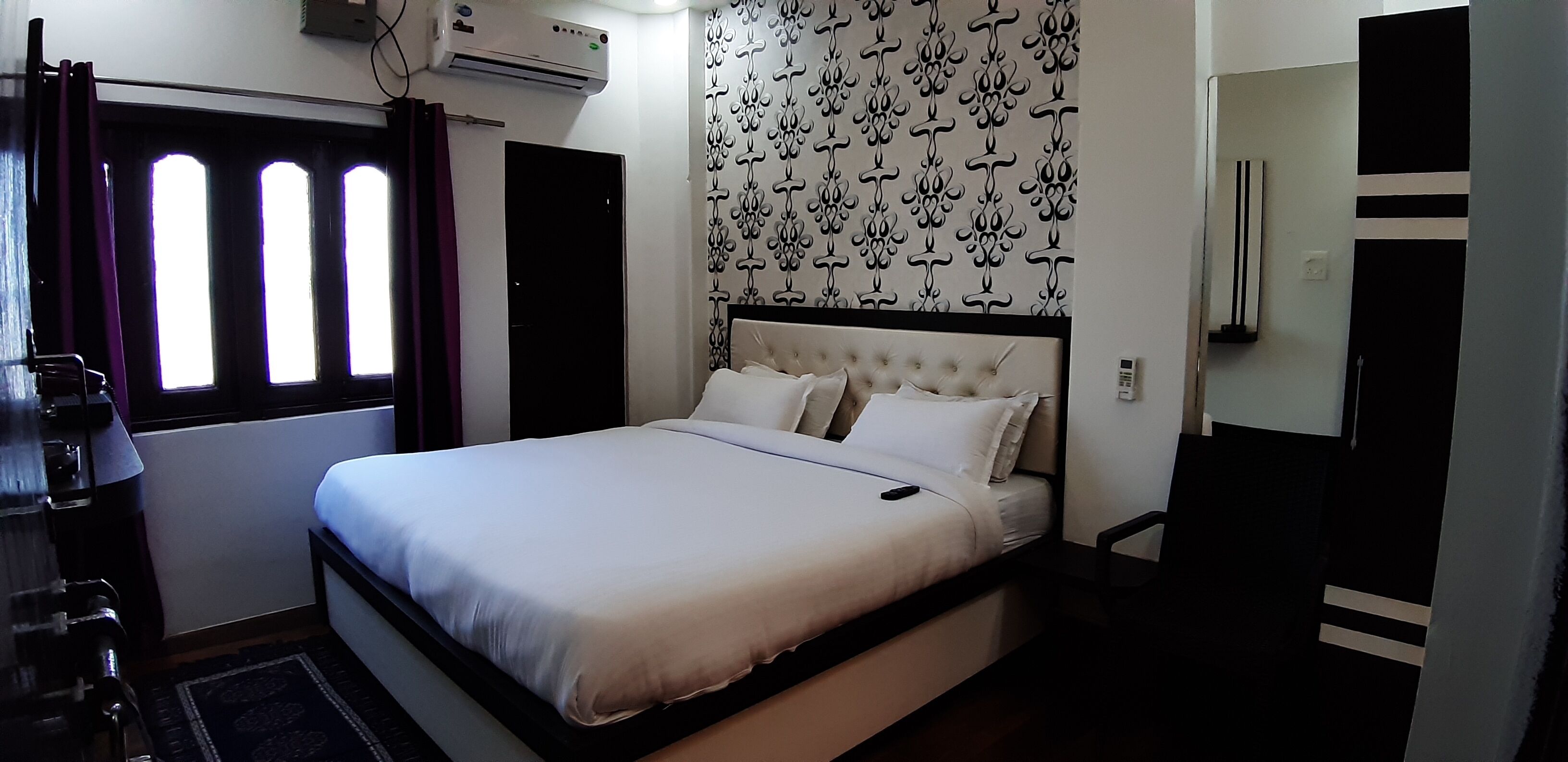 Une chambre d’hôtel avec un lit, une fenêtre avec des rideaux, un appareil de climatisation et un mur décoré de motifs.