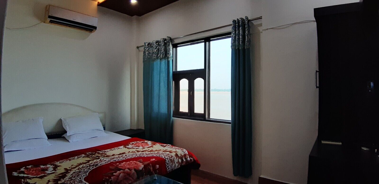 A bedroom with a bed, a window with curtains, an air conditioning unit, and a door.