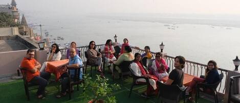 A group of people seated at tables on a terrace with a view of the sea.