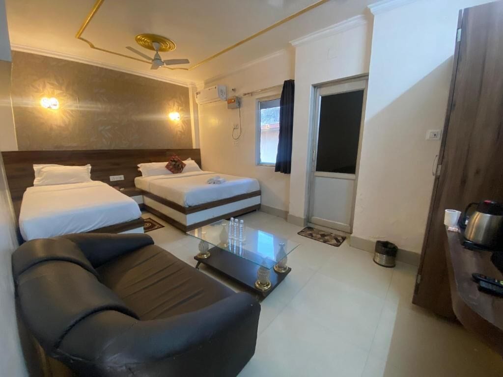A hotel room with two beds, a sofa, a glass coffee table, a ceiling fan, and a door leading outside.