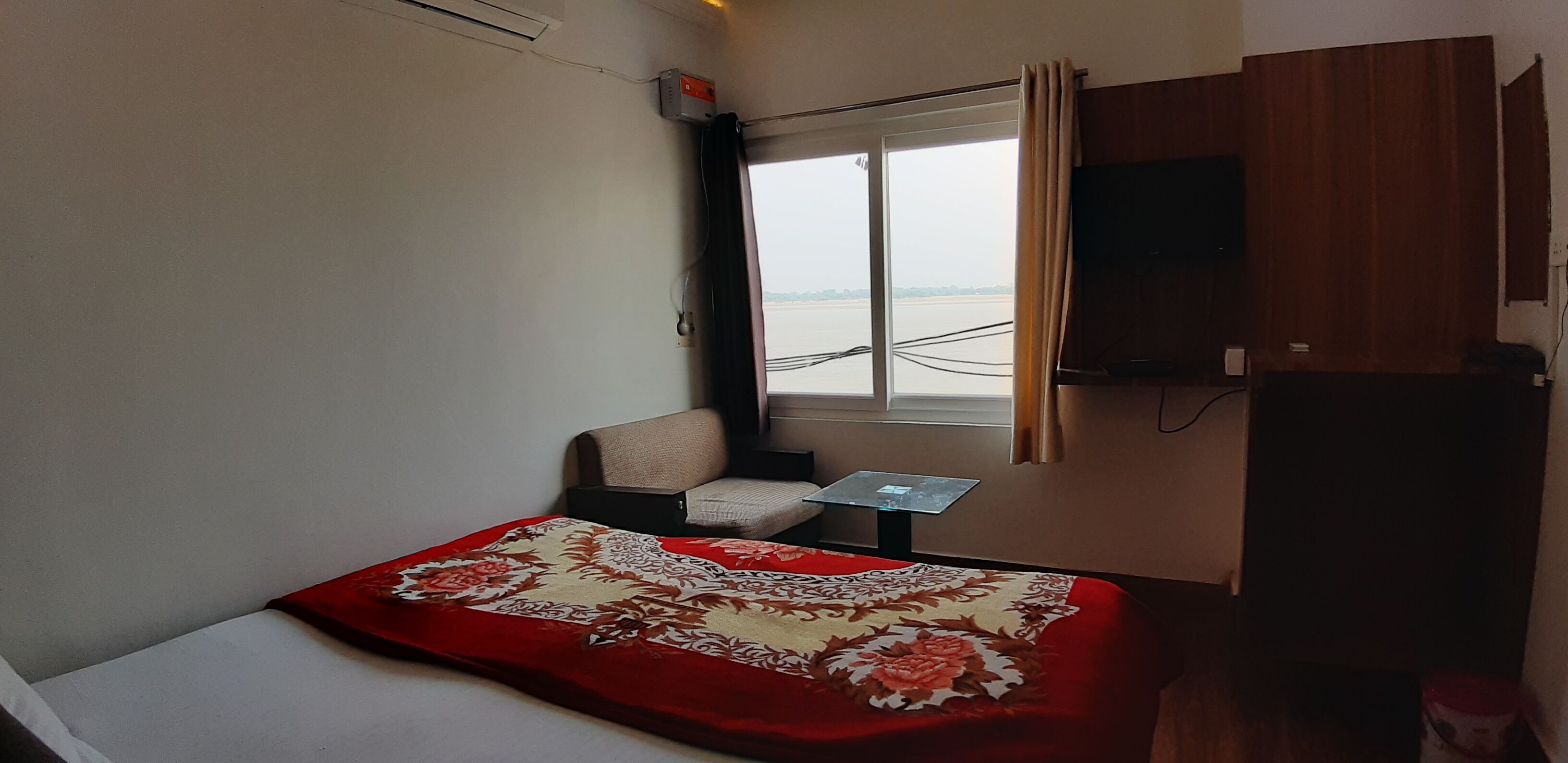 A hotel room with a bed, a small table, a TV, and a window with curtains.