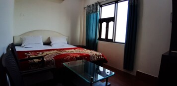 A room with a bed, a glass table, and a window with curtains.