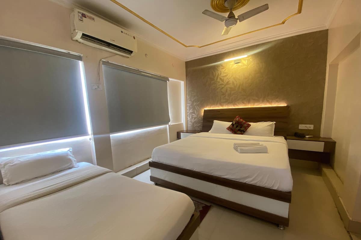 Habitació d'hotel amb dos llits, un ventilador de sostre, un aparell d'aire condicionat, una taula de nit amb una làmpada i una lluminària de paret.