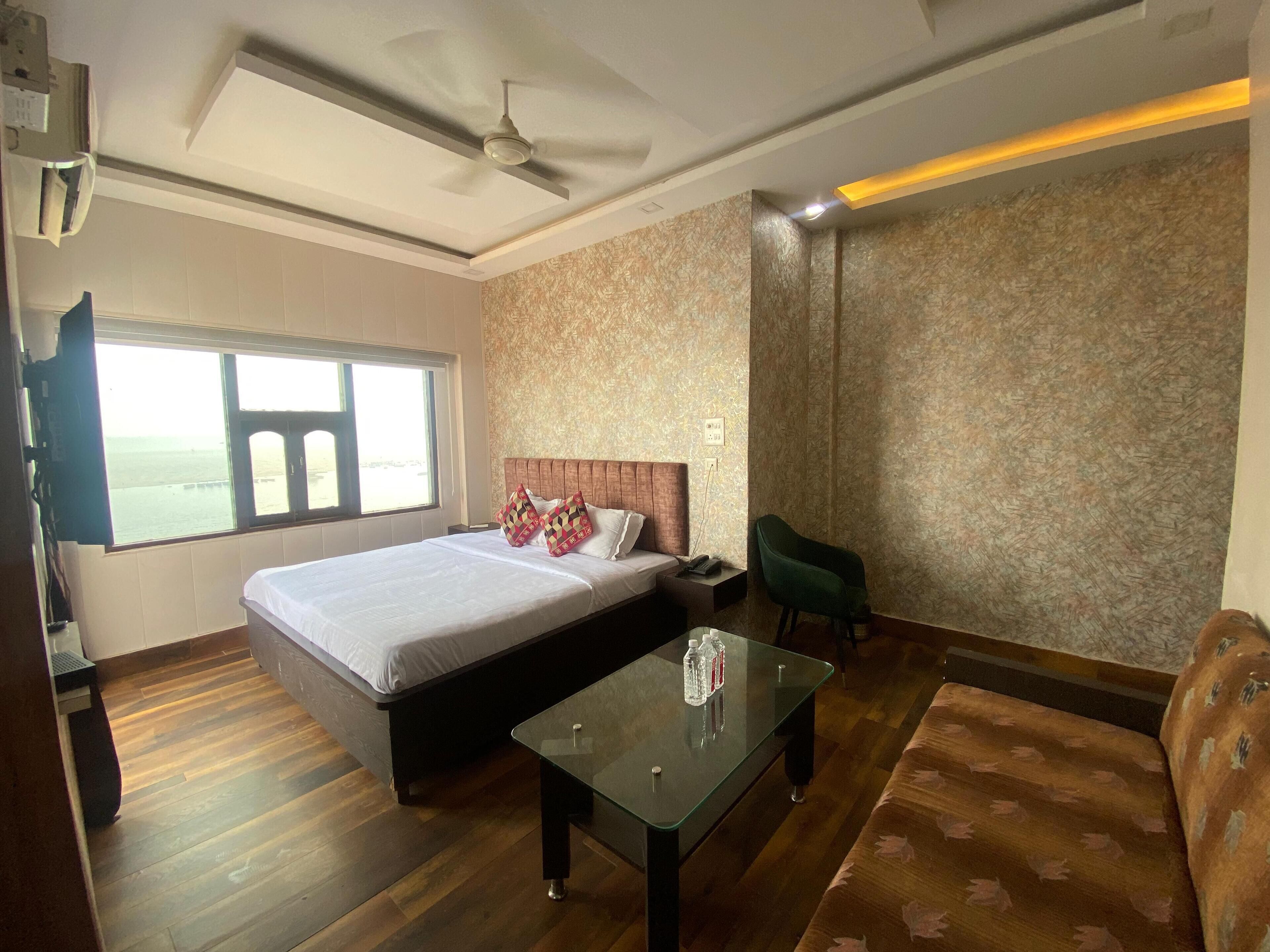 A hotel room with a bed, a glass coffee table, a green armchair, and a view of the sea through a large window.