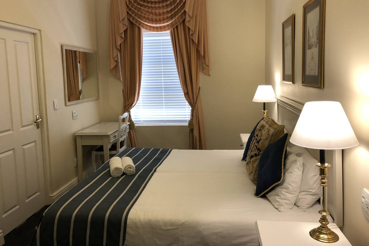 A hotel room with a bed, a desk, a chair, a lamp, and a window with curtains.