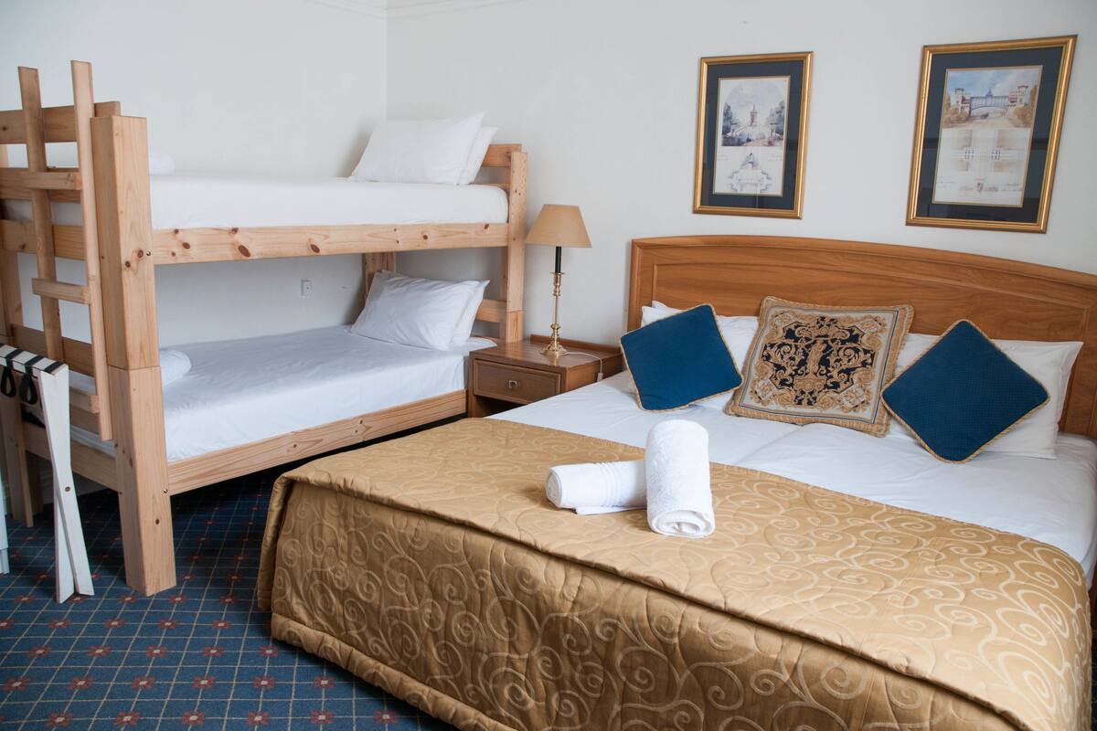 A bunk bed room with a wooden headboard, a bedside table with a lamp, and two framed pictures on the wall.