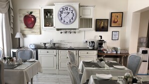Een eethoek met witte kasten, een grote wandklok, en een keuken voorzien van een koffiezetapparaat en waterdispenser.