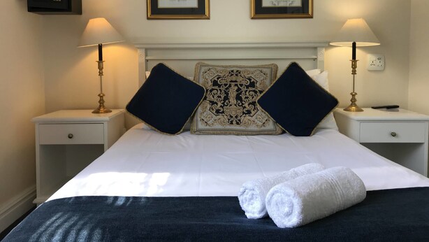 Een hotelkamer met een groot bed, twee nachtkastjes, twee lampen, twee ingekaderde foto's en een decoratief hoofdeinde.