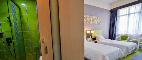 A hotel room with a shower, two beds, a nightstand, a lamp, and a window with curtains.