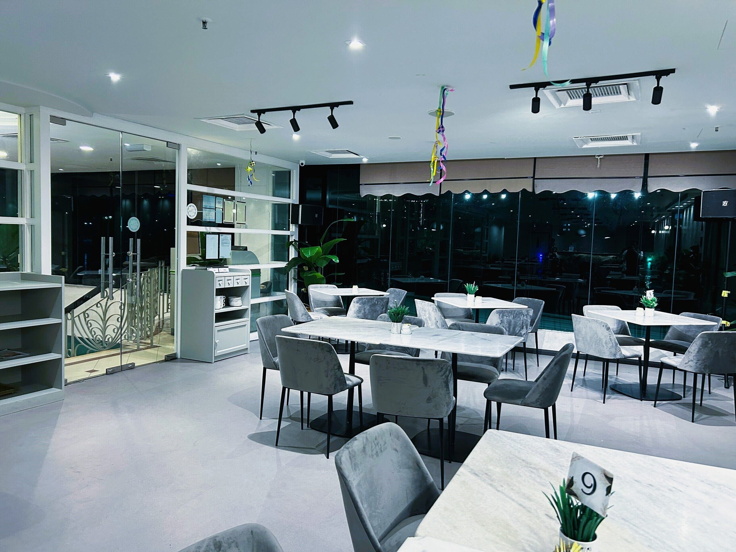 A modern dining area with white marble tables and chairs, a glass partition, and a staircase leading to an upper level.