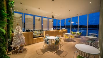 A modern restaurant with a view of the water, featuring a wooden counter, round tables, and chairs.