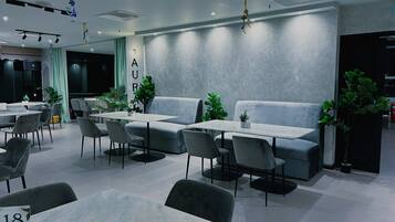 A modern dining area with tables and chairs, a sofa, and potted plants.