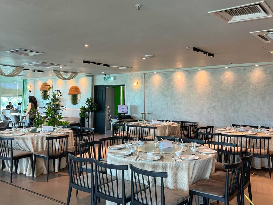 En rummelig restaurant med runde borde og stole, et grønt nødudgangsskilte, og udsigt udad.