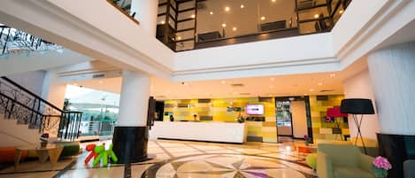 A spacious lobby with a central reception desk, a high ceiling with a skylight, and a modern staircase.