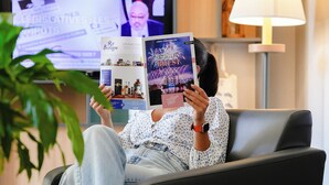 Eine Person sitzt auf einem Sofa in einem Raum mit Fernseher, Lampe und einem Regal mit Dekoration.