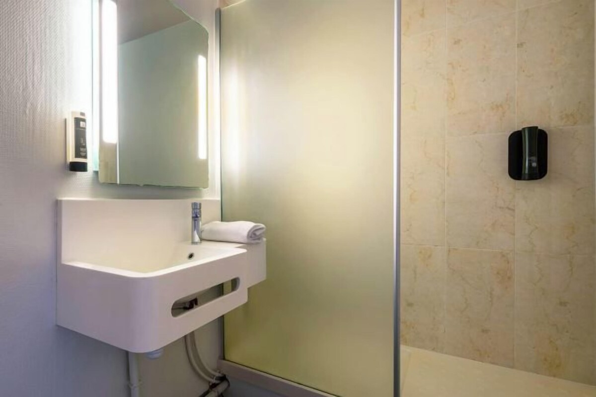A bathroom with a white sink, a mirror, a towel, and a soap dispenser.