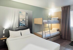Habitación de hotel con una cama grande, una cama nido, una mesita de noche, televisor montado en la pared y una ventana con cortinas.