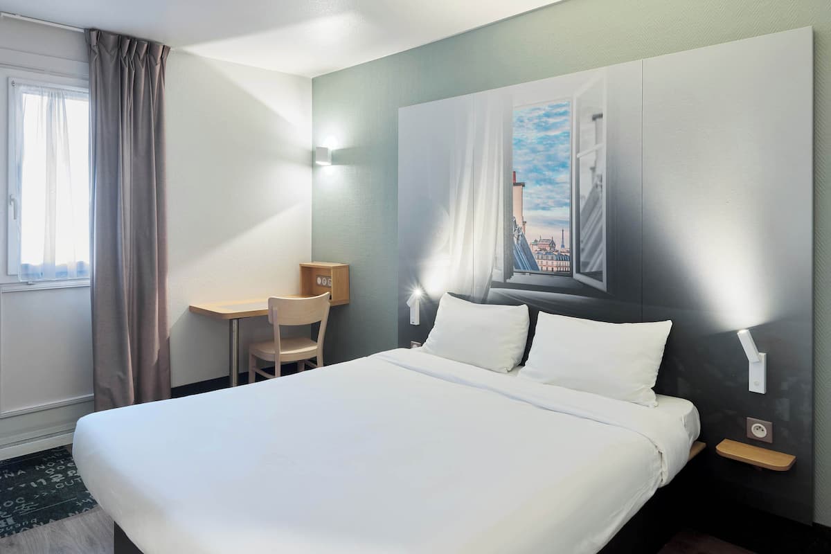 Quarto de hotel com uma cama grande, uma escrivaninha e uma cadeira.